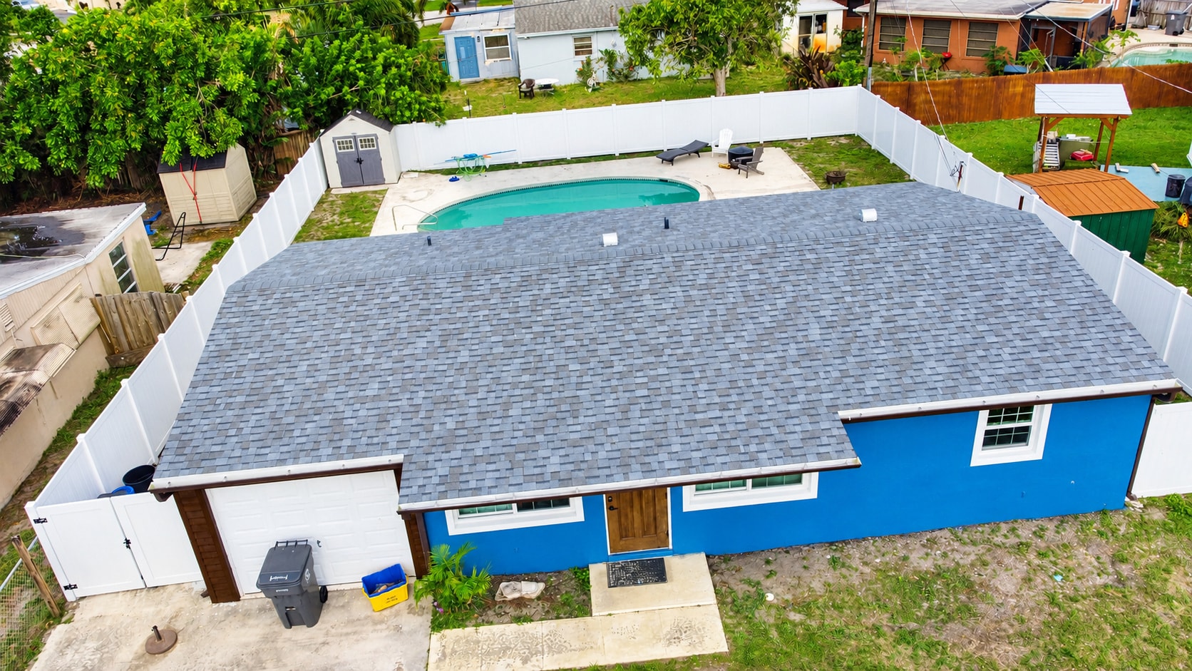 Aerial view of gray shingle roof on blue house with pool